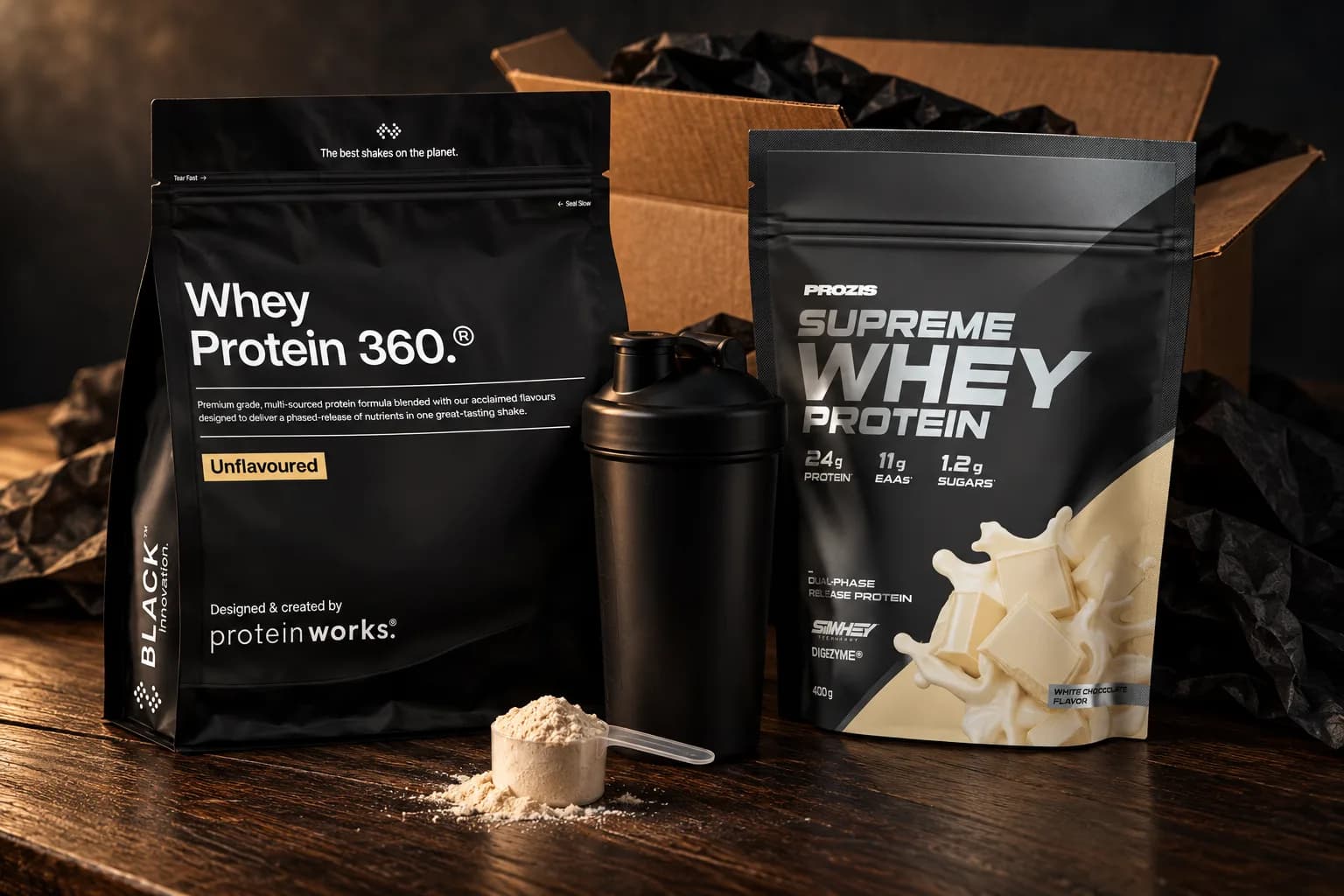 Pouches of Protein Works Whey Protein 360 Black Unflavoured and Prozis Supreme Whey White Chocolate with a black shaker and a scoop of powder, in front of an opened delivery box